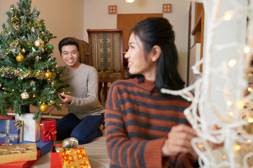 Happy young Asian man putting glowing lights on Christmas tree