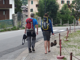 Fototapeta Włochy, Dolomity - turysta z plecakiem z obtartymi stopami idzie w klapkach, traperki trzyma w ręce obraz