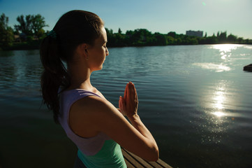 Close up portrait of attractive woman in meditating position on wooden log at the lake. Young girl doing yoga.