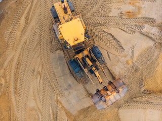 Yellow excavator or bulldozer works on construction site with sand, aerial or top view