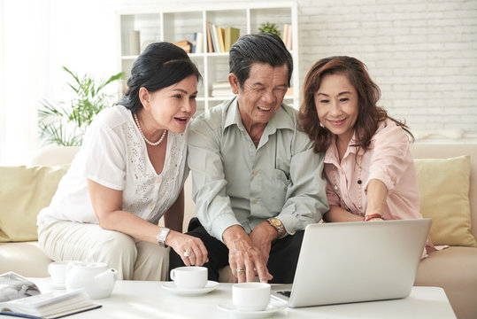 Laughing Senior Friends Watching Videos On Laptop Screen At Home