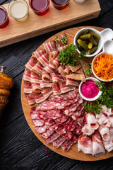 Sliced from different types of sausages and smoked meats with horseradish sauce, pickles and greens.