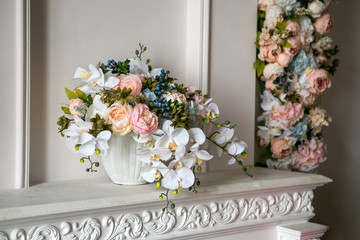 A bouquet of peonies, orchids and blueberries in a white flowerpot on a white fireplace in a classic style