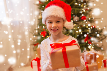 christmas, holidays and childhood concept - smiling girl in santa helper hat with gift box at home
