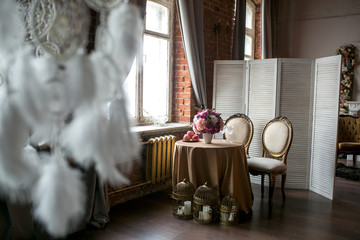 Dining table with classic chairs, a screen, fruit, a vase of flowers, candles and dream catchers in loft space, side view