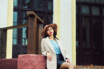 A young woman in a coat and a wide-brimmed hat on a city street .
