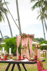 Table decor at a wedding party in burgundy and red hues. Wooden table stands on the air against the background of the wedding ceremony. Details - glasses, pomegranate, grapes, tablecloth, candles