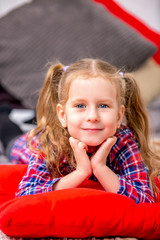 Happy cute young girl in a checkered blue-red dress lying on the bed and smiling