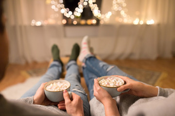 hygge, leisure and christmas concept - close up of couple drinking hot chocolate with marshmallow...