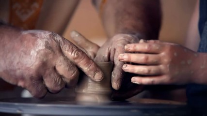 A potter teaches a student how to use potter's wheel
