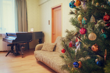 Beautiful festive decorated Christmas tree in living room interior with sofa, piano and window. Concept of new year holiday at cozy home. Vintage tone