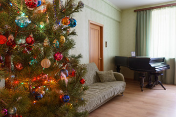 Beautiful festive decorated Christmas tree in living room interior with sofa, piano and window. Concept of new year holiday at cozy home