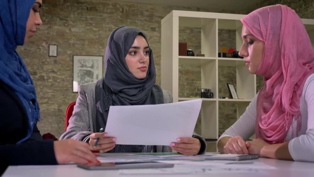 Cute working arab hijab woman are concentration and discussion at common desk, sitting, diverse communication, brick background indoor