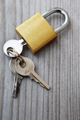 Golden padlock with three silver color keys on wooden background with copy space for text.