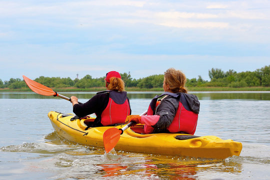 Two women paddle a yellow kayak on the Danube river. Water tourism and recreational at spring