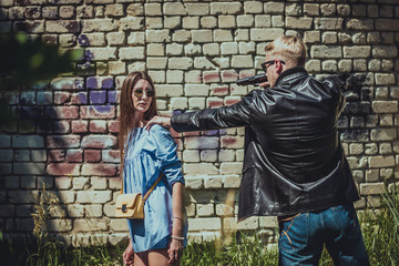 the robber on the street threatens the girl with a pistol and wants to take her bag from her. The bandit attacked the woman and wants to rob her.