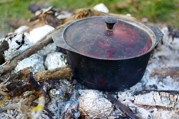 Potatoes in foil cooked on charcoal. Сauldron is heated on the fire. Cooking tourist food