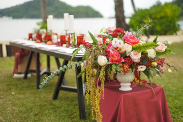 A wedding bouquet in a vase stands on a burgundy cube near the table, of flowers and greenery — roses, peonies, eustoma, orchids, eucalyptus, fern