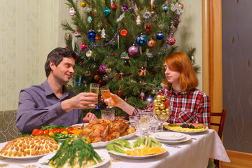 Handsome middle-aged man and beautiful young lady celebrating new year holidays with champagne siitting at festive table near decorated Christmas tree in living room interior. Cozy home concept