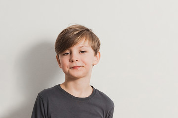 a portrait of cute boy pulling faces, snooty look, dark grey shirt, white wall. Copy space for your text and design