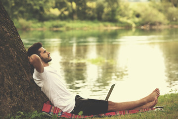 man using a laptop computer on the bank of the river