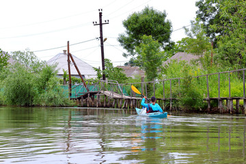 Man paddling in blue kayak. Kayaking in channels of Danube river in Vilkovo town in Ukraine on background of street