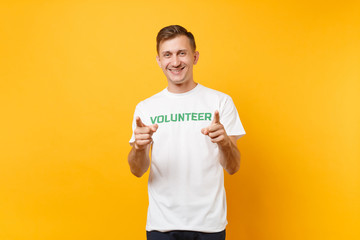 Portrait of happy smiling satisfied young man in white t-shirt with written inscription green title volunteer isolated on yellow background. Voluntary free assistance help, charity grace work concept.