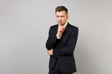 Serious young business man in classic black suit shirt say hush be quiet with finger on lips, shhh...