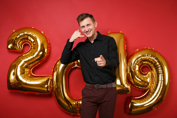 Merry handsome young man in black shirt celebrating holiday party standing isolated on bright red...