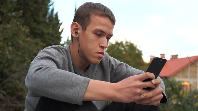 Teenager in headphones using a smartphone. Outside the city. Summer evening