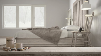 Wooden vintage table top or shelf with candles and pebbles, zen mood, over blurred contemporary bedroom, bed with wooden headboard, minimal architecture interior design