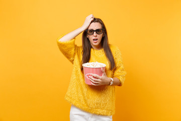 Concerned frustrated young girl in 3d imax glasses putting hand on head watching movie film holding bucket of popcorn isolated on bright yellow background. People sincere emotions in cinema lifestyle.