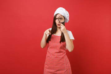 Housewife female chef cook or baker in striped apron white t-shirt toque chefs hat isolated on red wall background. Housekeeper woman hold and look through magnifying glass. Mock up copy space concept