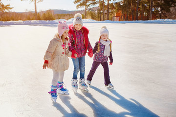 Three little girls skate on the ice. Vacations and holidays in nature