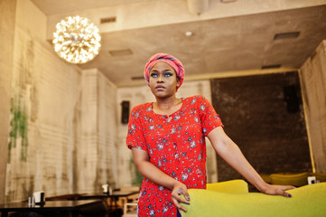 Stylish african woman in red shirt and hat posed indoor cafe.