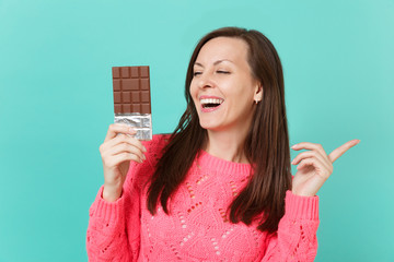 Smiling young woman in knitted pink sweater pointing index finger aside, holding in hand chocolate...