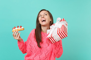 Funny woman in pink sweater looking up, hold eclair cake, red striped present box with gift ribbon...