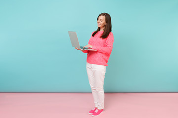 Full length portrait of woman in knitted rose sweater, white pants using laptop pc computer...