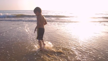 Slow motion - A child 3-5 years old running freely while the camera chase him and he laughs, in a sunny day in the beach 