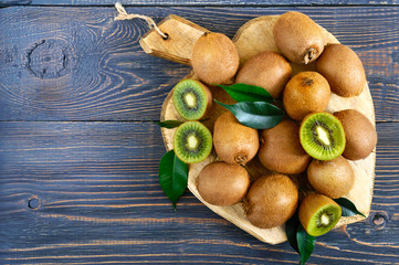 Ripe fruits of kiwi whole and halves are scattered on a cutting board with an old knife on a wooden table. Top view.