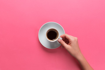Minimalistic style woman hand holding a cup of coffee on pink background. Flat lay, top view