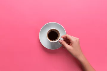 Zelfklevend Fotobehang Minimalistic style woman hand holding a cup of coffee on pink background. Flat lay, top view © sosiukin