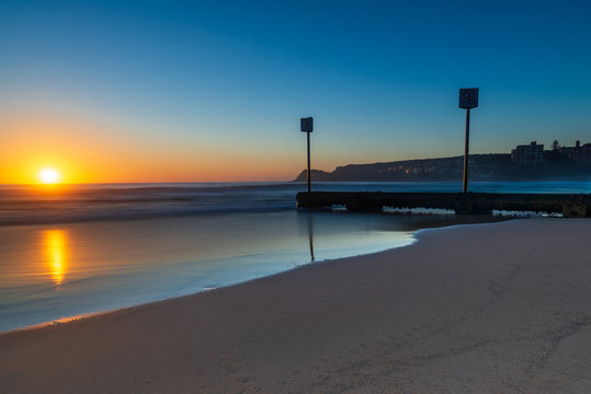 Sunrise over iconic Manly Beach, Sydney Australia. Clear skies and the storm water pipes lead the long exposure image.