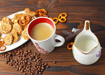 A cup of coffee, grains of coffee and cookies on a wooden table.