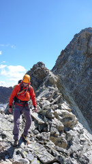 mountain climber hiking along a sharp and rocky mountain ridge under a blue sky