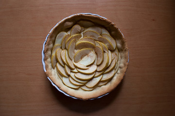 Half baked pie filled with sliced apples in floral rosette shape isolated on wooden board from a high angle view
