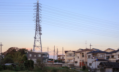 High voltage power lines run from tower in residential neighborhood at sunset