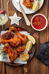 Tasty appetizing baked chicken legs served with spices, rosemary and cranberries on wooden background table. Christmas dish. Copy space.