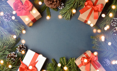 Gifts, for branches and pine cones form a frame with fairy lights on blue background. Christmas background, top view