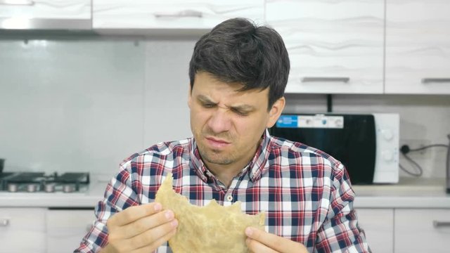 Young man in a plaid shirt eats a big cheburek with disgust and spits food.